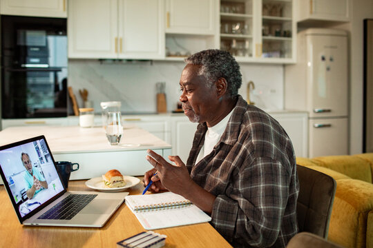 Senior man having telehealth video call at home kitchen