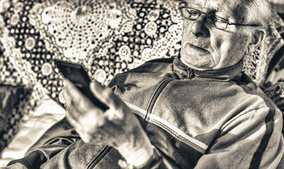 Elderly man with glasses looking at mobile phone at home