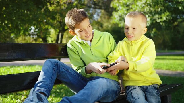 Two brothers sitting on park bench, arguing and fighting over a smartphone. Concept of sibling rivalry and technology use