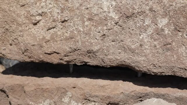A close-up shot of two ancient stone blocks coming together over metal pins, completing a structural repair at a historical site.