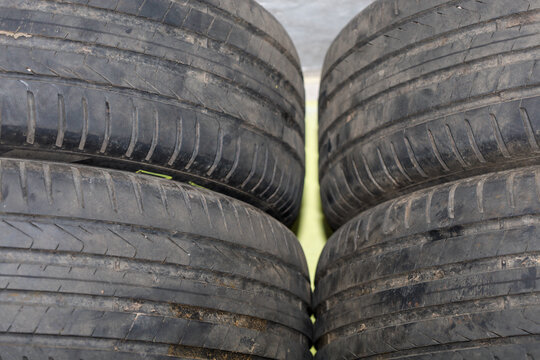 Four used car tires with worn-out treads are stacked together for storage or recycling purposes. A detailed view of the rubber showing signs of wear and dust emphasizes the importance of timely tire r