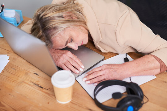 Fatigued Professional Resting on Laptop At Desk With Notebook And Coffee Cup