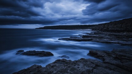 Obraz premium Dark dramatic storm clouds gather over a rocky coastline with rough ocean waves crashing ashore