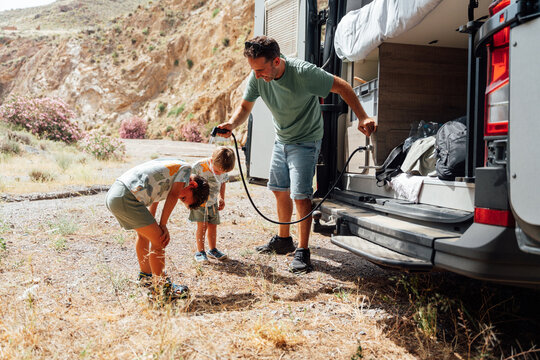 Father and children cooling down by camper van on summer road trip
