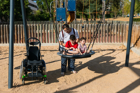 Mother pushing children on accessible swing in playground