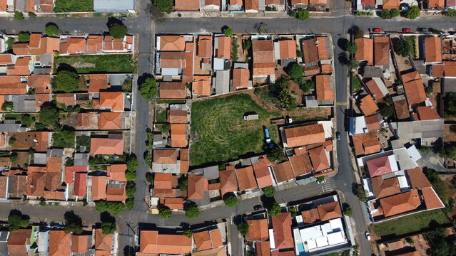 Aerial view of a residential neighborhood with red tile roof houses and an empty urban lot in the center of a small Brazilian city.