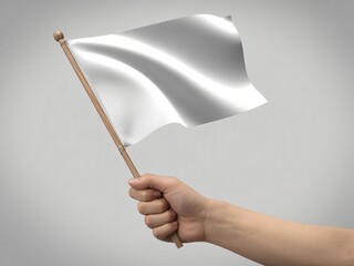A hand holds up a plain white flag that is waving gently in the air. The flag is attached to a wooden stick and stands out against a neutral grey background.