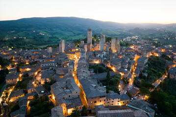 Obraz premium Aerial night view of San Gimignano illuminated after sunset, with its medieval towers and historic center glowing against the Tuscan landscape. A dramatic perspective of this iconic Italian hill town