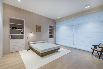 Obraz premium A bedroom features a bed without bedding, light wood flooring, and built-in bookshelves. A floor lamp provides light in the corner. A chair sits by the wall near a large window