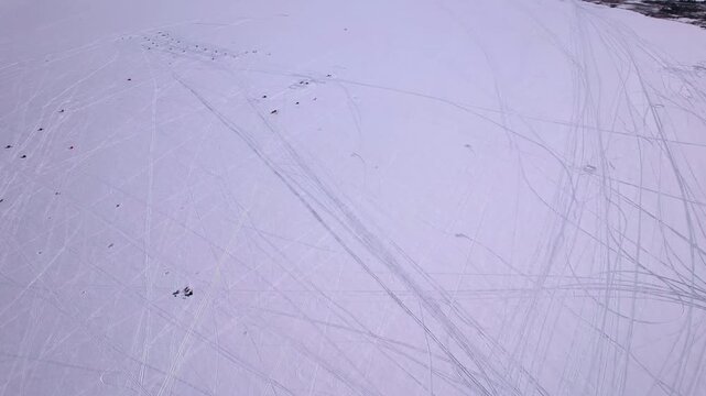 Aerial drone footage of snowmobiles intricate curved tracks patterns textures on fresh winter snow under bright sunny sunlight. Ice fishing sport on frozen lake Simcoe, Cook&rsquo;s Bay, Innisfil, Canada.