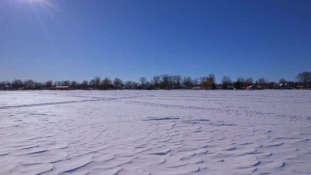 Aerial drone view at snowmobile, atv or ice fishing sled and snowdog tracks along the winter snowy lake Simcoe. Tourists and winter active recreation during ice fishing season. Blue sky.