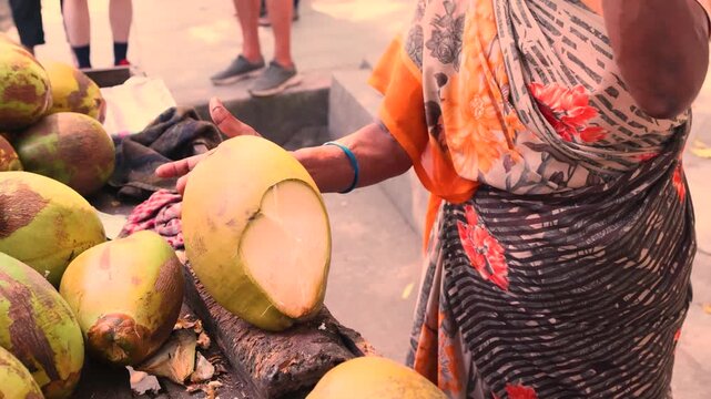 Close up of hands of a woman chopping a coconut using a large machete Traditional method for preparing fresh coconut water Common in Indian, Asian and Indochina cultures showing local lifestyle 