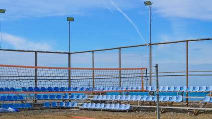 Fototapeta premium Beach volleyball court with blue seating and net under clear sky