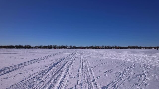 POV driving plate of driving snowmobile, atv or ice fishing sled and snowdog tracks along the winter snowy lake Simcoe. Tourists and winter active recreation during ice fishing season. Blue sky.