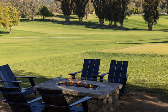 Chairs around a rectangle stone firepit next to a luxury golf course