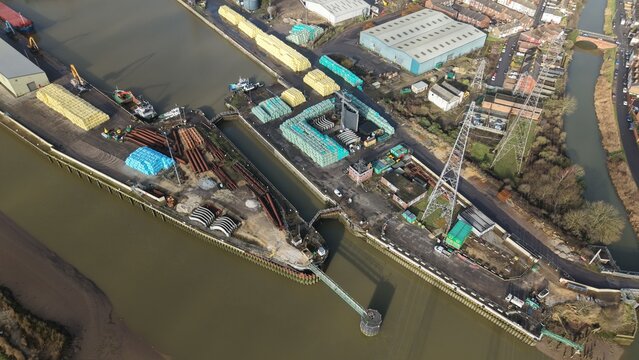 Aerial view of the port with stacks of timber and metal, cranes, and industrial buildings lining the waterway, Boston, England, United Kingdom.