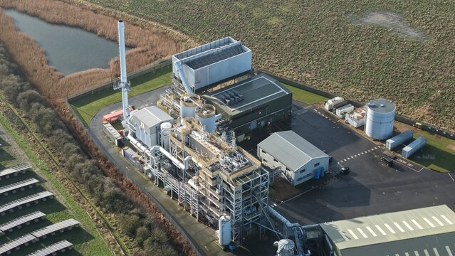 Aerial view of the Biomass Nr. 3 power plant complex standing starkly against the muted landscape, framed by a tranquil pond and solar panels, Boston, United Kingdom.