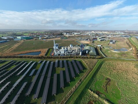 Aerial view of solar panels gleaming under a bright sky, juxtaposed with the Biomass Nr. 3 power plant, Biomass Nr. 3 power plant, Boston, United Kingdom.