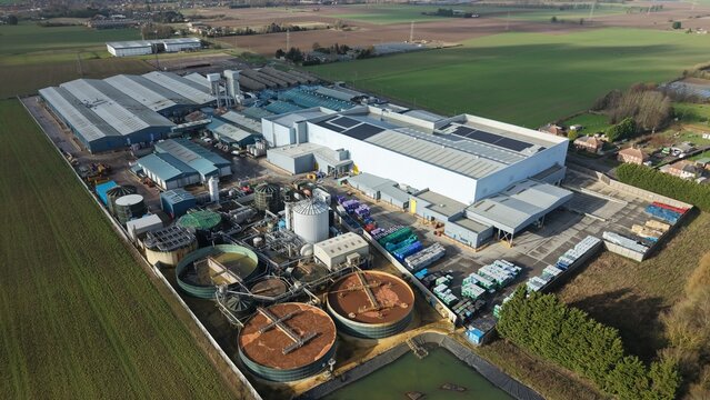 Aerial view of a sprawling industrial complex where the sharp lines of warehouses meets the organic curves of settling ponds, Princes Factory, Sutton Bridge, United Kingdom.