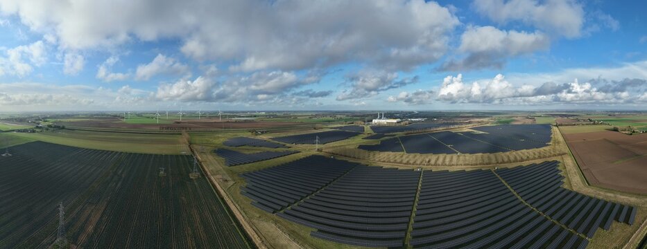 Aerial view of a solar farm's dark panels contrast with the patchwork of green and brown fields under a vast cloudy sky, Sutton Bridge, Sutton Bridge, United Kingdom.