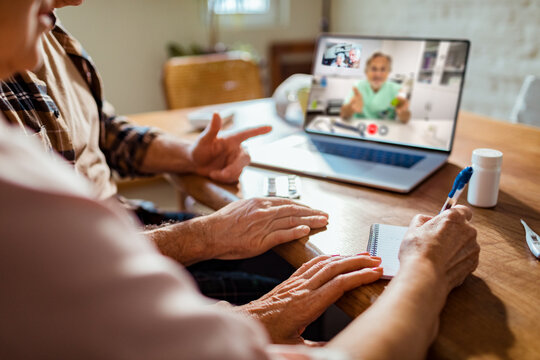 Senior couple taking notes during telehealth video call at home