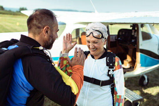 Happy senior woman high fiving skydiving instructor at airfield