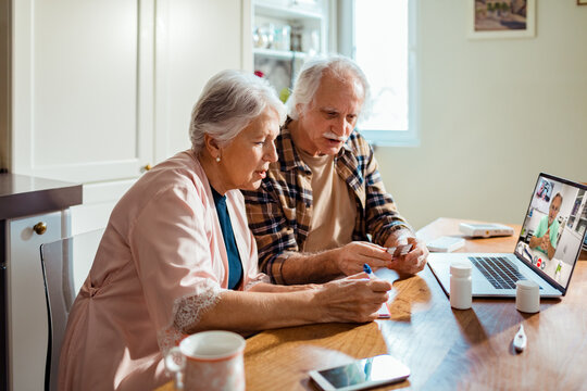 Senior couple consulting doctor online at home kitchen table