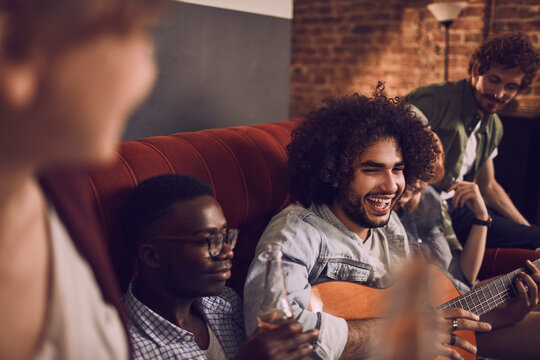 Young friends playing guitar and singing at a cozy house party