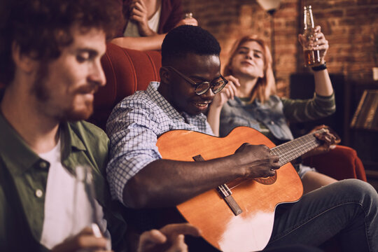 Young friends playing acoustic guitar at home party