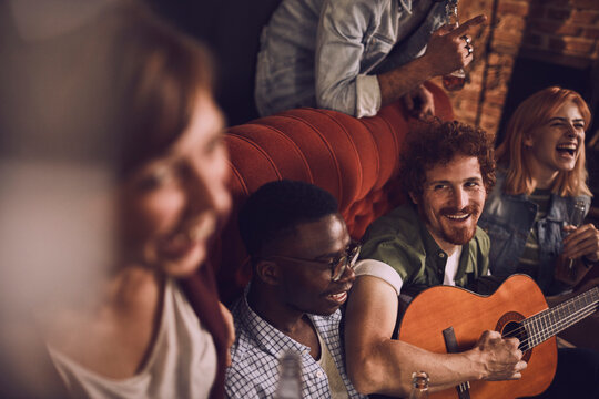 Friends laughing and singing with guitar at house party
