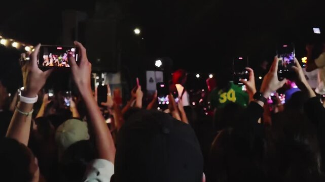 Montevideo, Uruguay: January 19 2026: Rear view medium shot video of audience with mobile phone at free outdoors at "rueda de candombe", a public outdoors music festival at ciudad vieja neighborhood, 