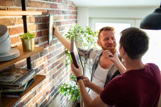 Two men hanging picture frames on a brick wall at home