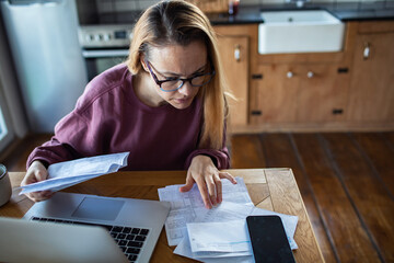 Obraz na płótnie Canvas Woman reviewing household bills at home kitchen table