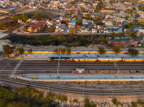 Aerial view of a train on parallel tracks cutting through the town, with buildings clustered in the background, bathed in the warm glow of the setting sun, Sambhar, Rajasthan, India.