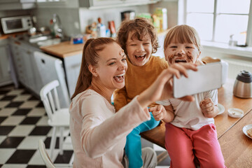 Mother and children taking a messy selfie in home kitchen