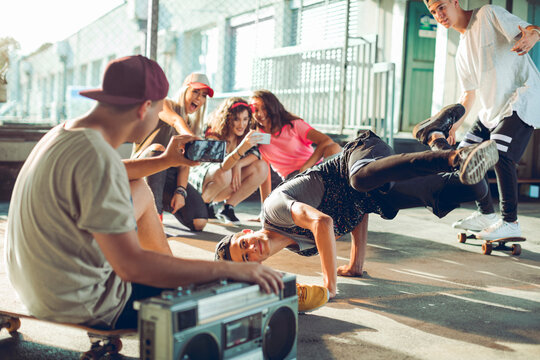 Teen friends filming breakdancer at urban skatepark