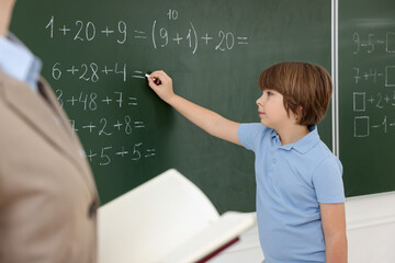 Schoolboy doing math on chalkboard in classroom
