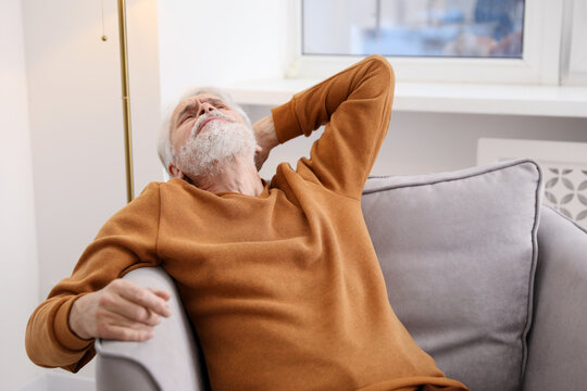 Unhappy senior man feeling fatigue on sofa at home