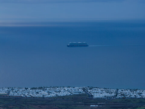 Aerial view of a cruise ship sailing on the tranquil, deep blue sea near the coastal town, Tias, Lanzarote, Canary Islands.