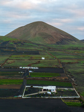 Aerial view of dark volcanic earth meeting the green slopes under a muted sky, Tias, Lanzarote, Canary Islands.