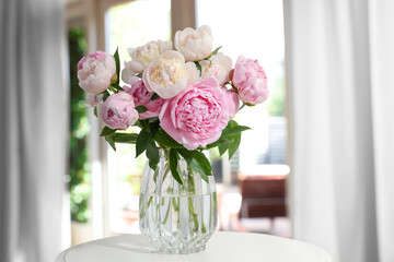Bouquet of beautiful peonies in glass vase on table near window