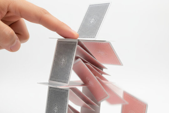 Hand touching falling house of cards illustrating structure collapse, fragility, financial risk and business failure concepts