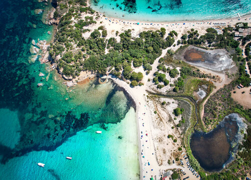 Aerial view of turquoise waters meeting the sandy beach, lush vegetation contrasting with the dark lagoons, creating a mesmerizing coastal panorama, Corse, Corse du sud, France.