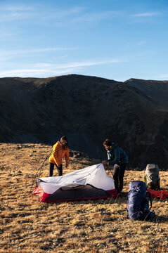 Supportive friends collaborating to raise tent before sunset