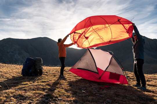 Focused campers stretching rainfly over tent in open highlands