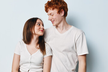 Fototapeta premium Young couple standing against light background looking at each other smiling casual clothing together. Man and woman with red hair and brown hair posing and showing affection.
