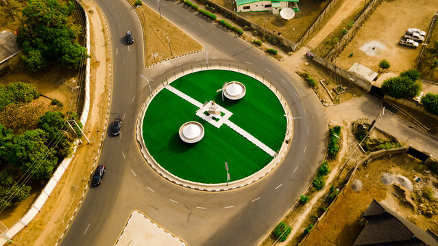 Aerial view of a vibrant green roundabout with striking white lines and monuments amidst the bustling roads, Ilorin, Kwara, Nigeria.