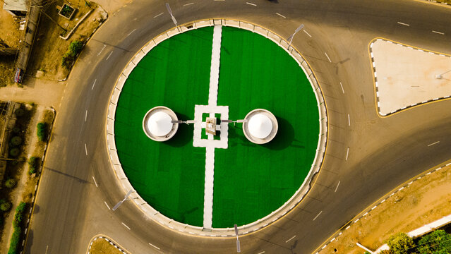 Aerial view of a vibrant green roundabout with white architectural features stands out against the dark asphalt roads, Ilorin, Kwara, Nigeria.
