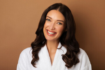 Portrait of attractive young European woman in bathrobe with nude makeup posing on beige studio...