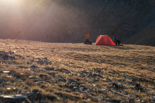 Distant campers setting red tent on quiet alpine grassland
